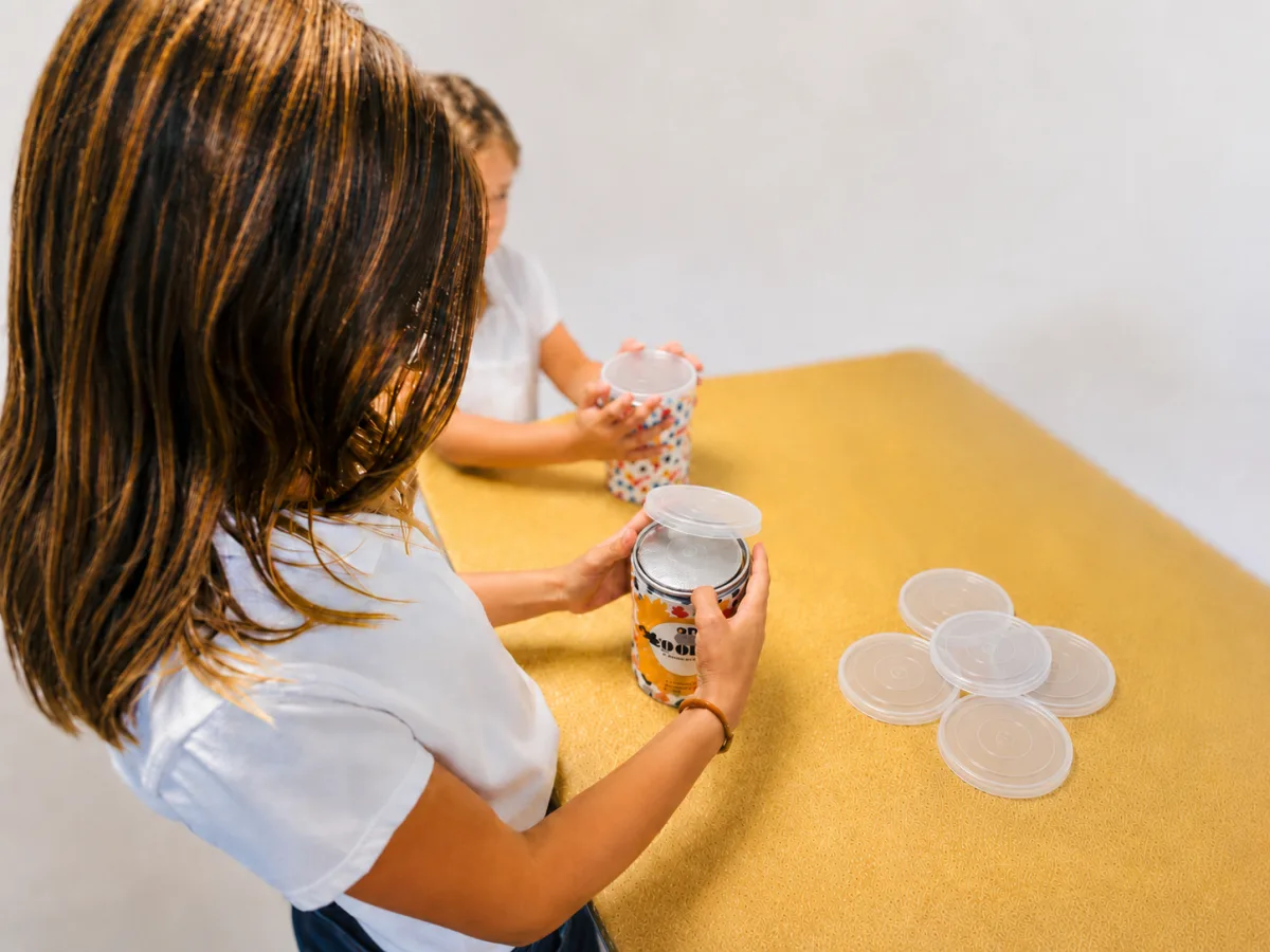 Overhead view of clear snap lids being pressed onto filled tins by hand.